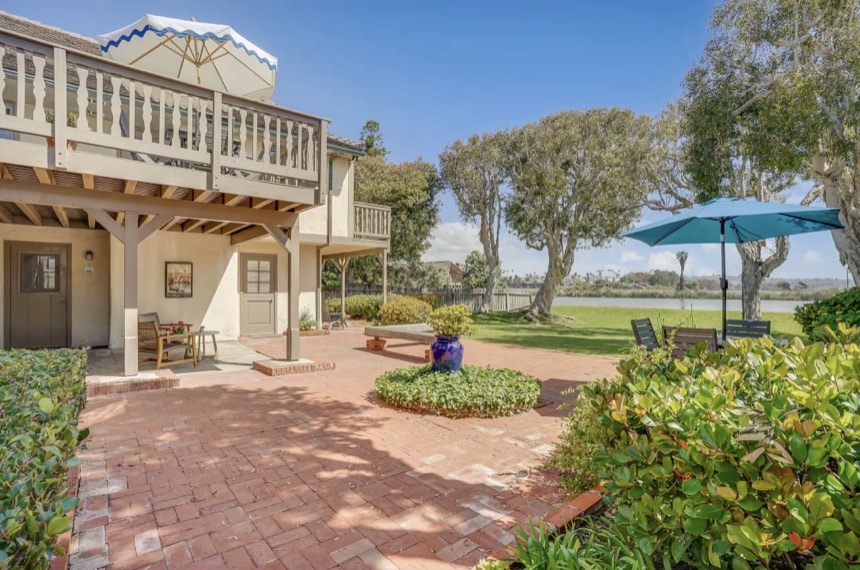 The brick patio opening onto the lawn, teal umbrella up, the lagoon beyond